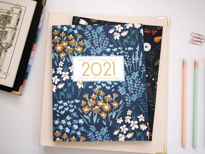 A 2021 planner on a stack of notebooks with pencils and paper clips beside it