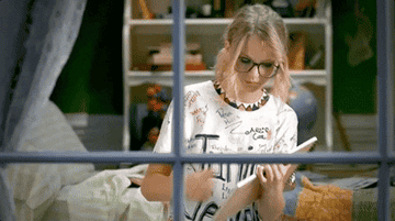 a gif of taylor swift holding up a sign that reads &quot;you ok?&quot; in the &quot;you belong with me&quot; music video
