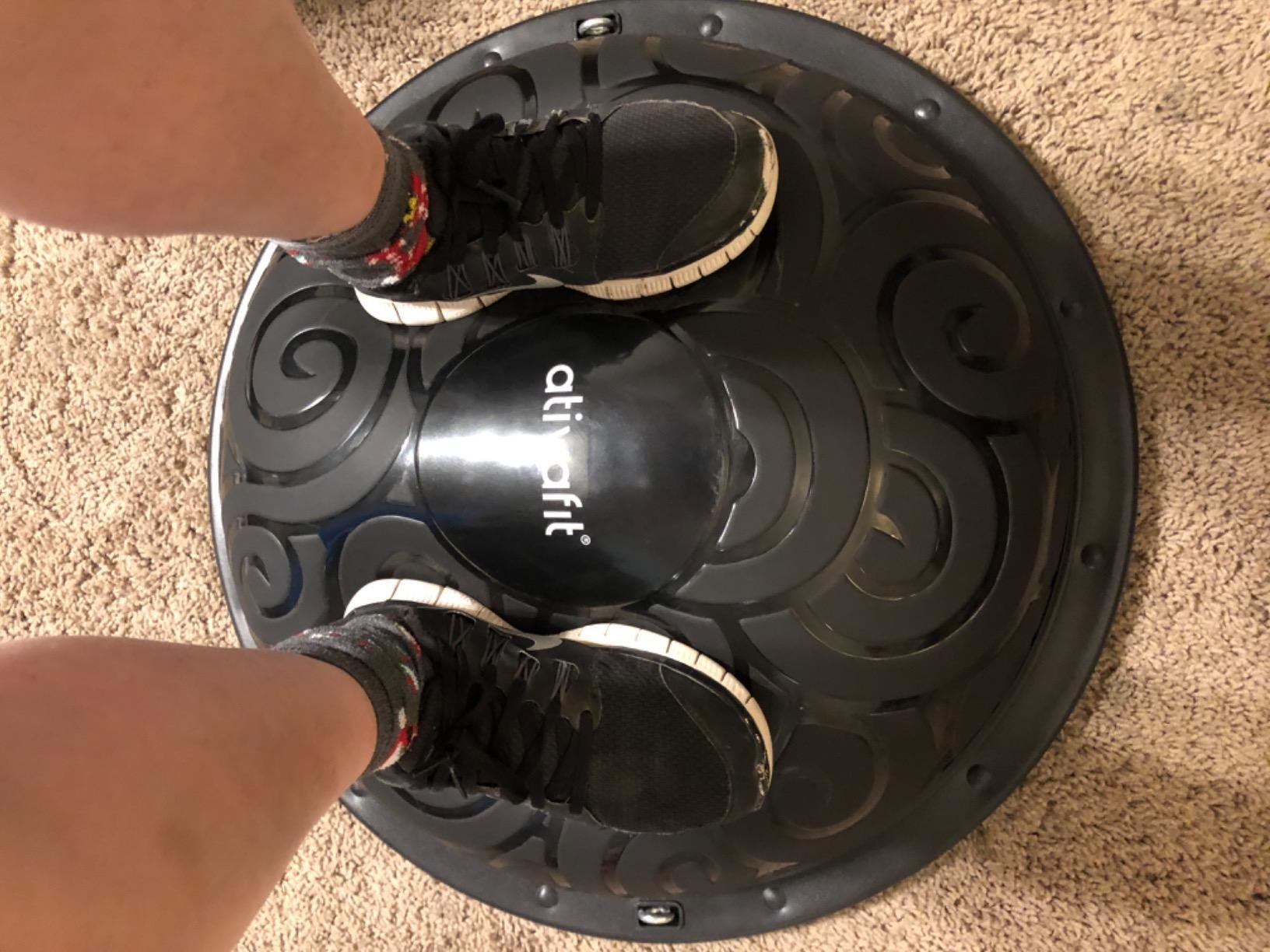 Reviewer stands on black balance ball trainer placed on tan carpet
