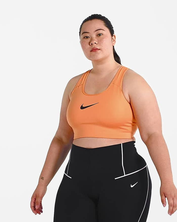 Model wears peach Nike medium-support sports bra with black high-rise leggings