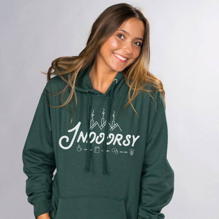 a model in an evergreen sweatshirt with the word &quot;indoorsy&quot; on it and some home-themed icons