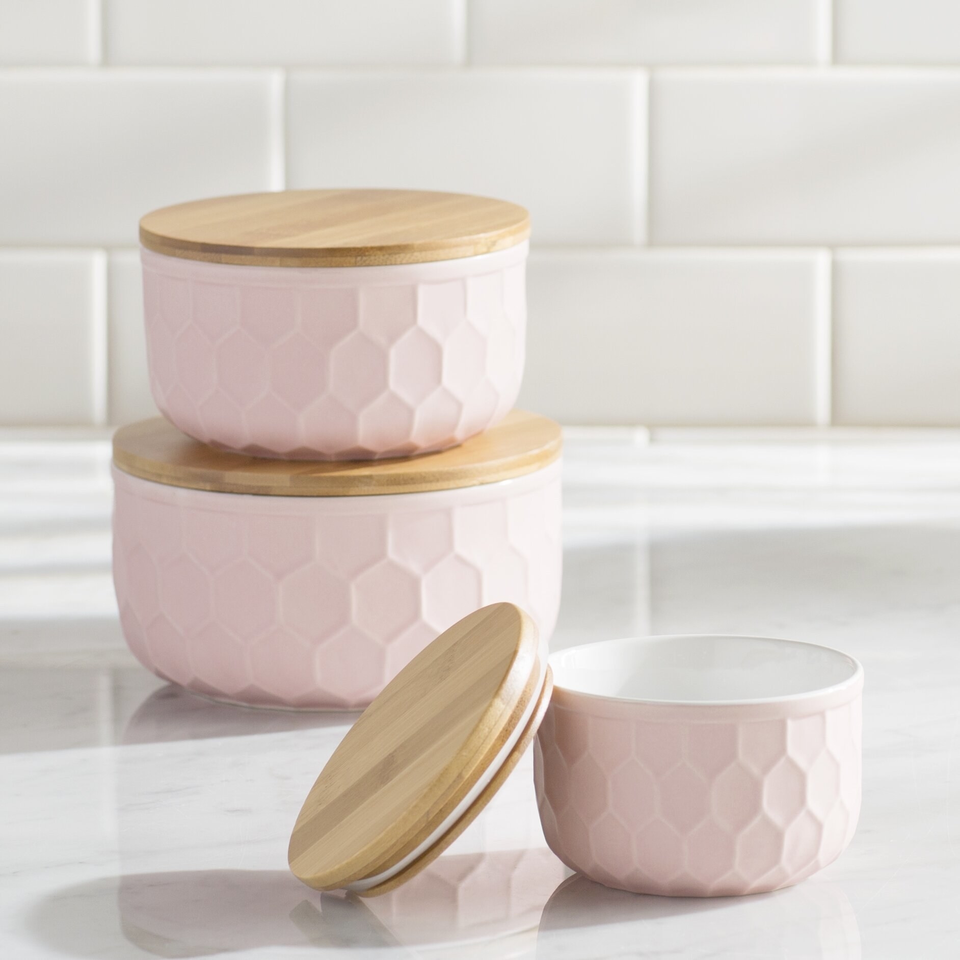 Three pink honeycomb canisters with brown wooden tops on a kitchen counter 