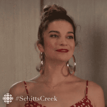 Annie Murphy in the TV show &quot;Schitt&#x27;s Creek&quot; wearing huge gold hoop earrings and rolling her eyes and head with confidence