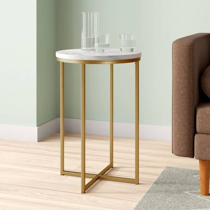 Gold and white side table next to a couch with glasses of water on it