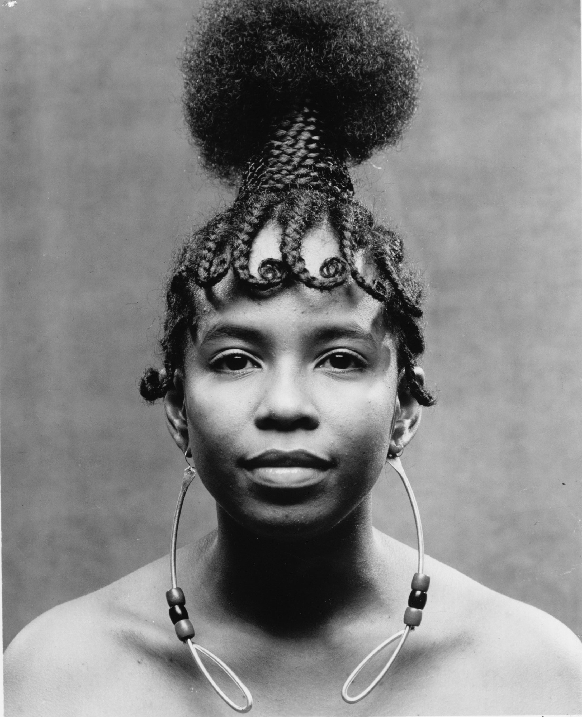 A woman with long earrings, braids, and her hair done up, with her shoulders bare