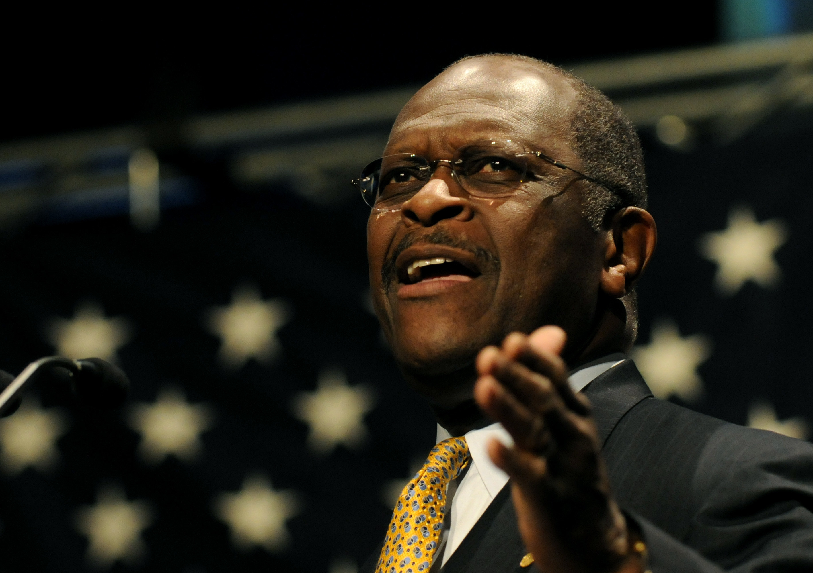 Cain onstage among stars, gesturing as he speaks