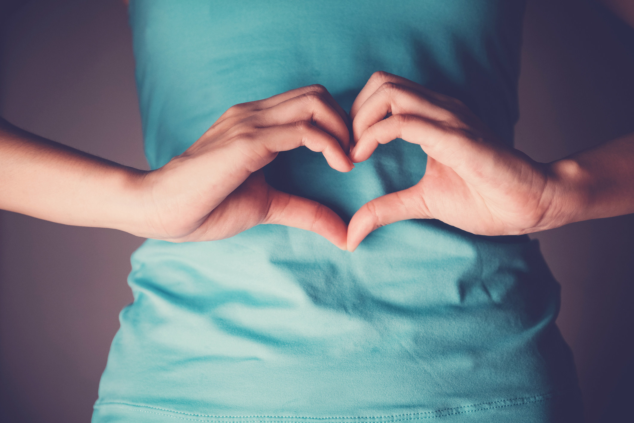 Woman making a heart with her hands over her stomach.