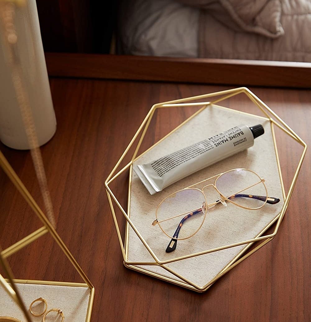 The tray on a bedside table holding a tube of hand cream and glasses