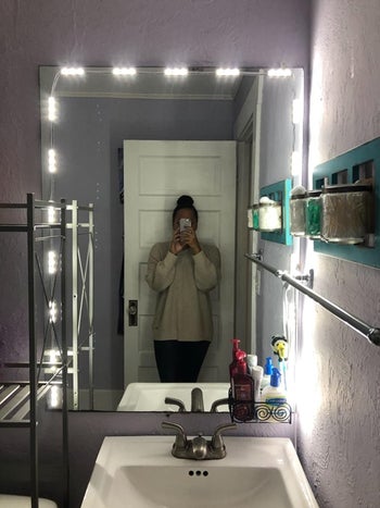 Reviewer takes selfie in front of bathroom vanity mirror adorned with lights