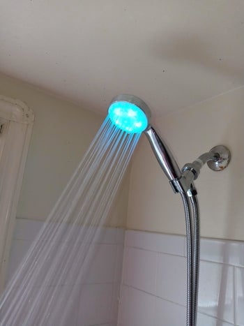 Blue-light coming out of LED showerhead in white-tiled shower