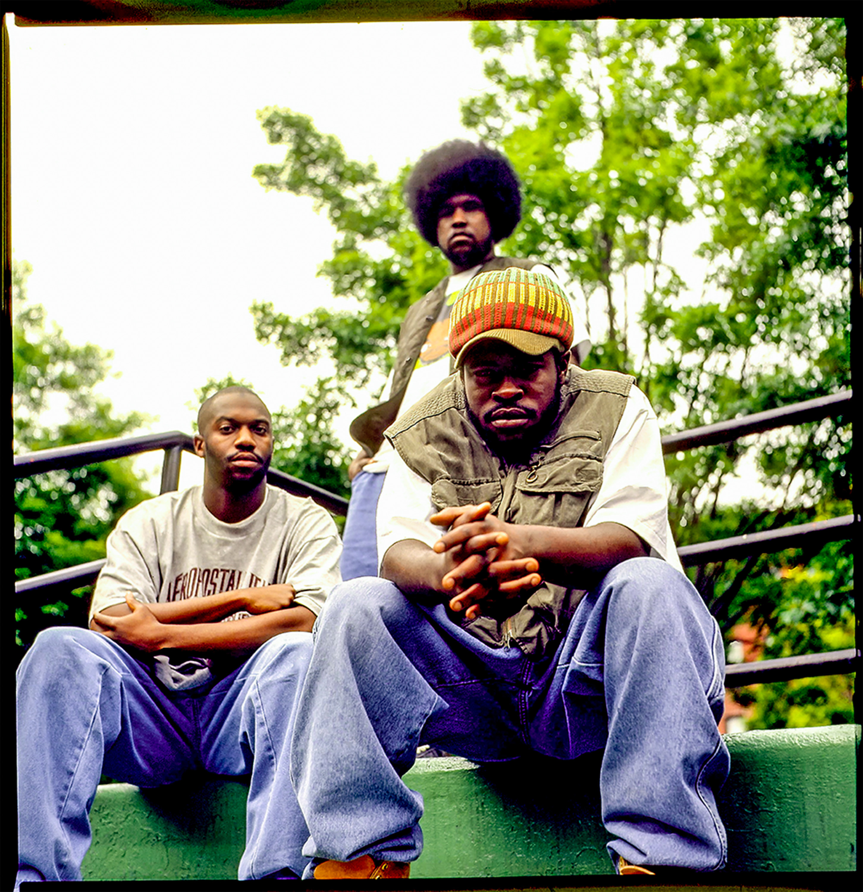 The three members of the Roots outside, looking at the camera, wearing t-shirts and jeans