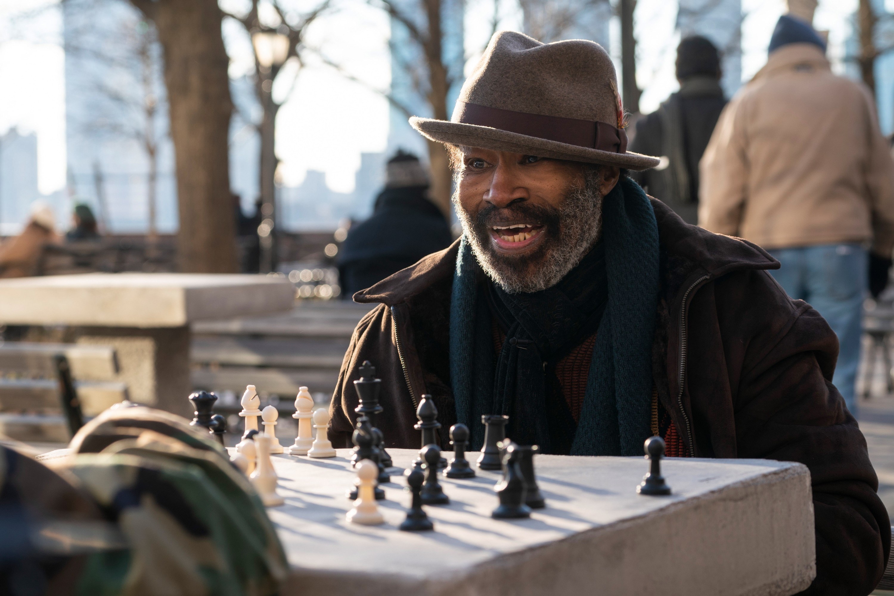 Chisholm in a fedora and jacket playing chess outdoors in NYC