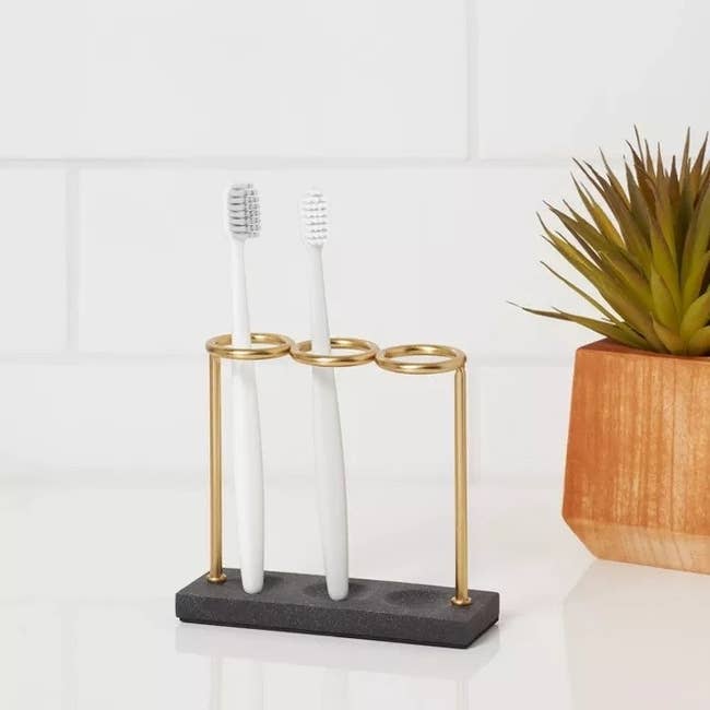 Gold toothbrush holder with three toothbrush slots on a white countertop