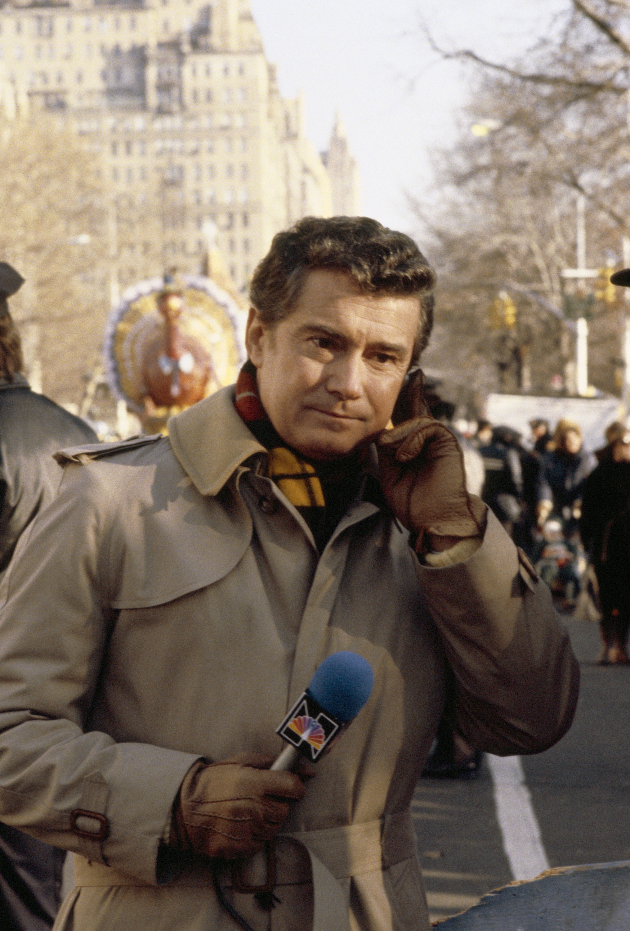 Philbin in a trench coat with a microphone during a parade