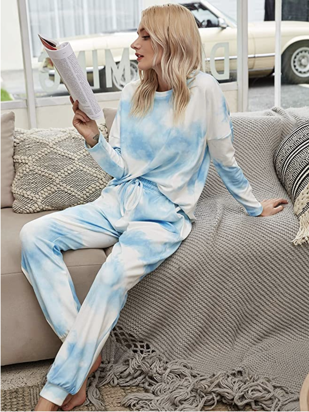 person wearing a tie dye pj set sitting on the couch reading a book