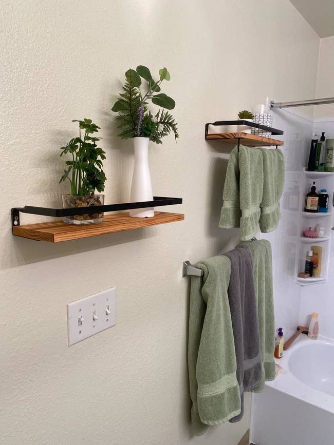 Brown floating shelves with white plant vases and green towels hanging below