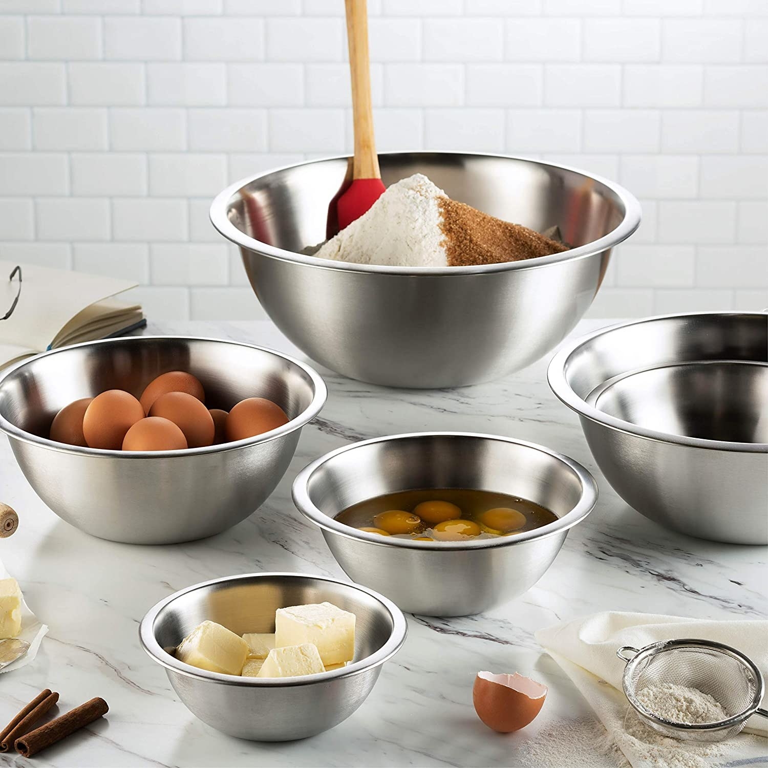 Six stainless steel bowls in different sizes on a counter with different food in each one