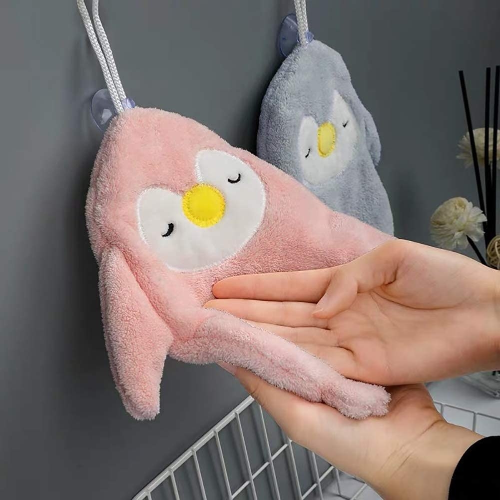 Model dries hand on pink penguin-shaped towel above sink