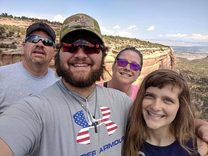 A family of four stands in front of a canyon, smiling for a selfie