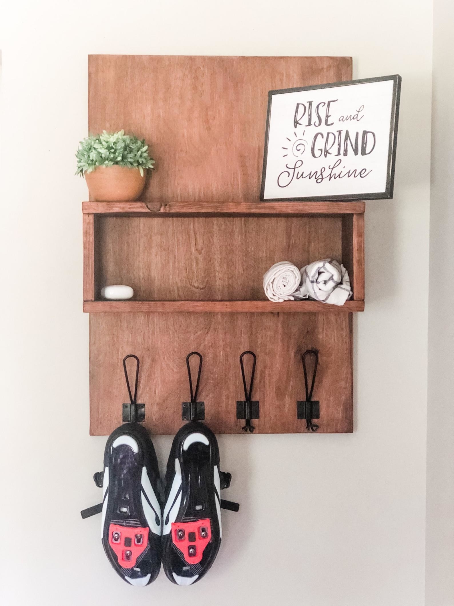 A wood shelf with hooks for the Peloton cleats hangs on the wall.