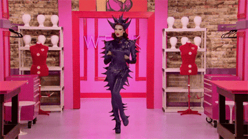 Drag queen Miss Fame wearing a purple spiky bodysuit and matching headpiece