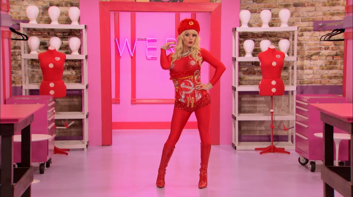 Drag queen Katya wearing a red bodysuit and corset styled with Russian insignias, and matching headpiece