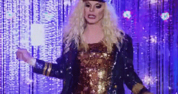 Drag queen Katya wearing a gold sequin leotard, blue sequin captain&#x27;s jacket, captain&#x27;s hat, and a shark on her leg
