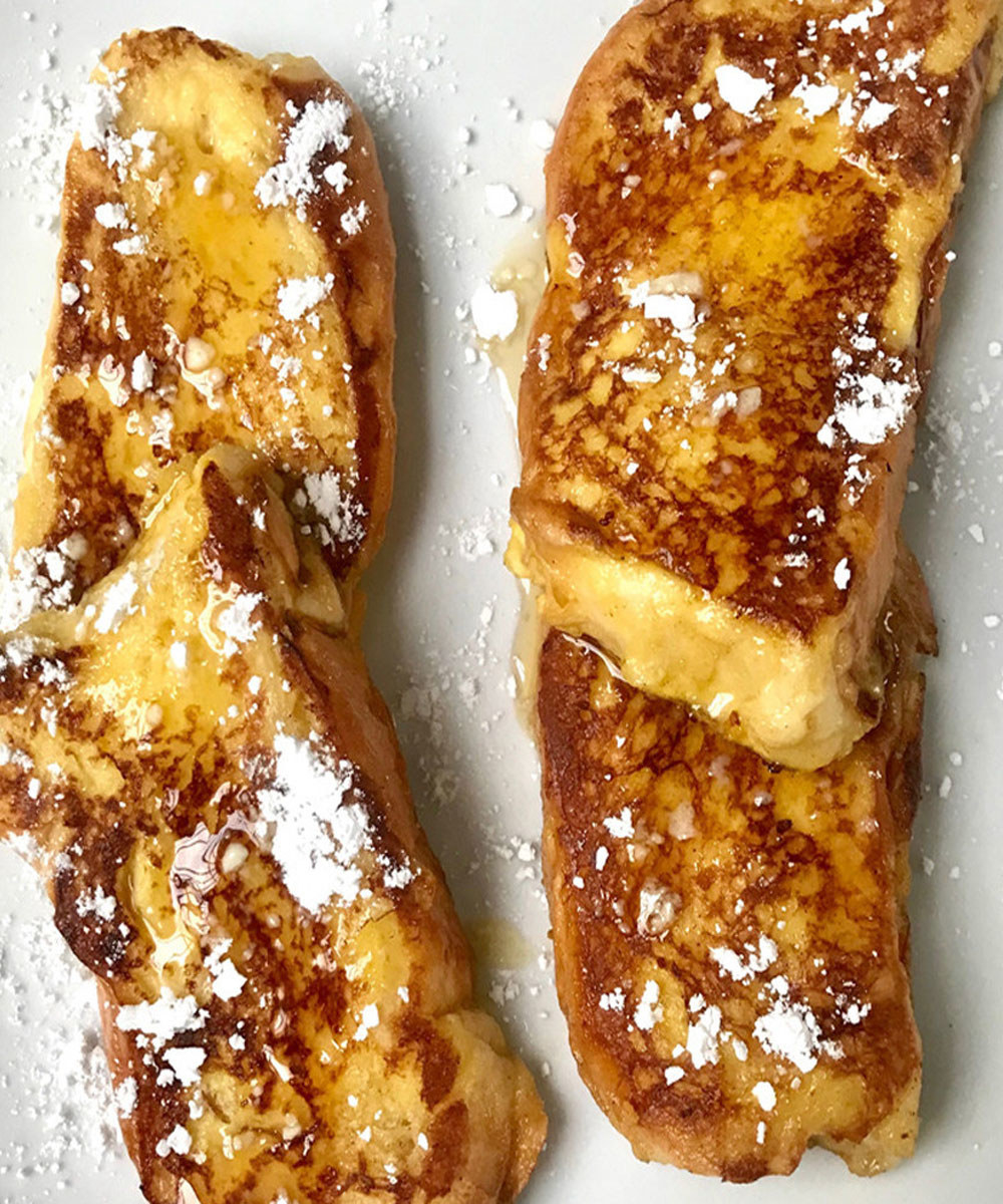 Four pieces of challah French toast topped with powdered sugar and syrup.