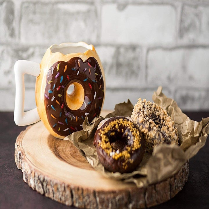 A donut-shaped coffee mug on a wooden tray with donuts