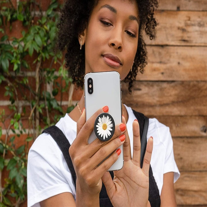 A person holding up their phone that has a round phone grip stuck to the back
