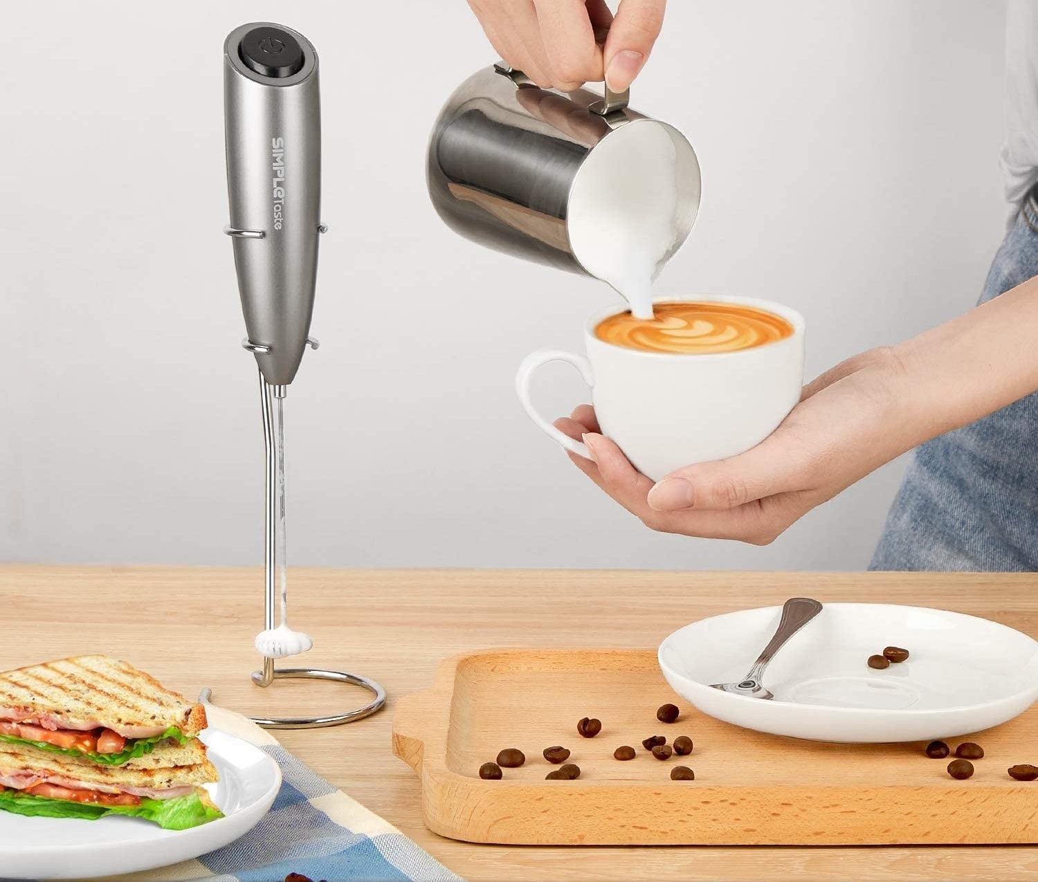 milk frother on stand next to person pouring milk into a drink