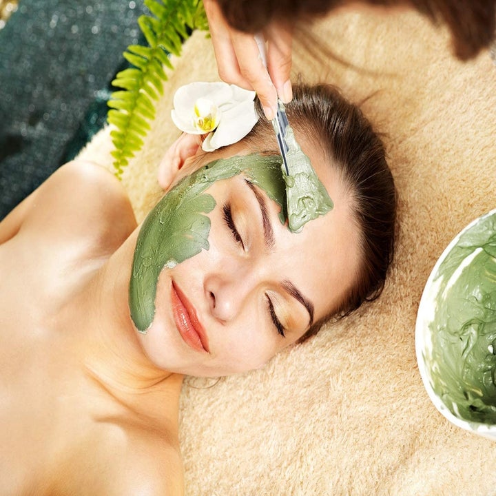 A person applying a mud mask to someone's face with a silicone spatula