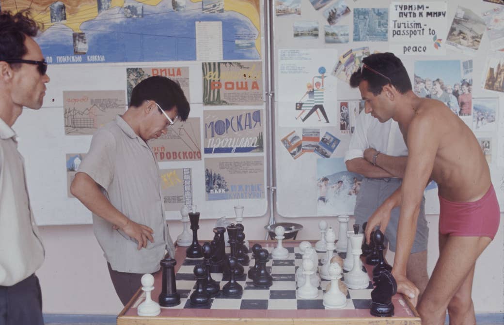 A man in a polo shirt plays large-scale chess with a man in pink bathing shorts