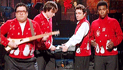A gif of four SNL cast members jamming out in christmas sweaters