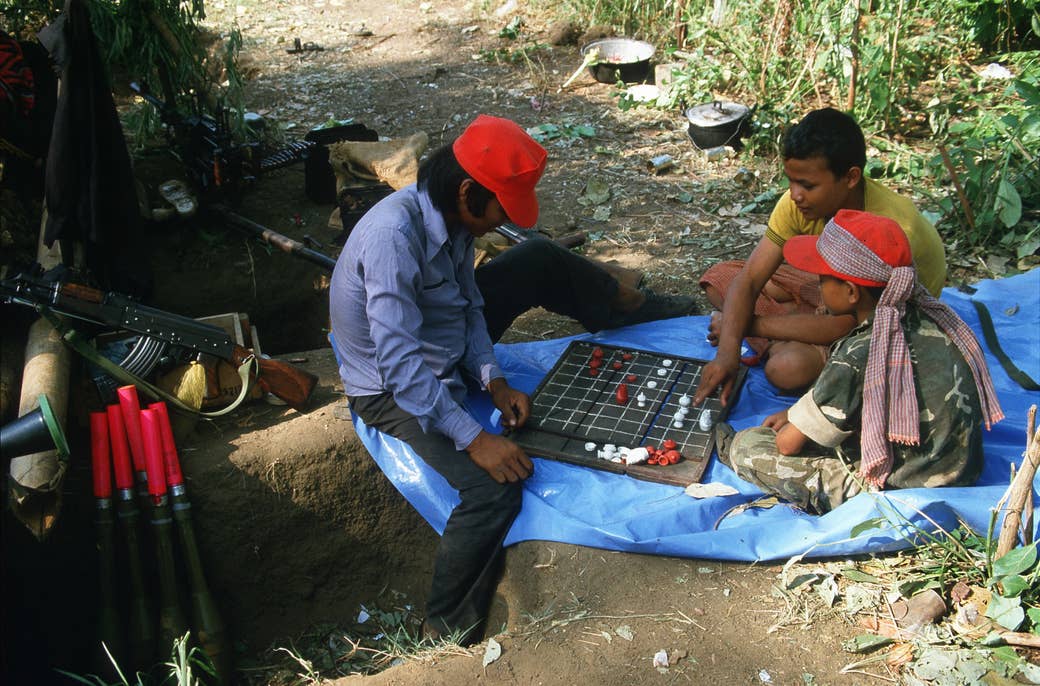 Three child soldiers play chess on a blue tarp outside