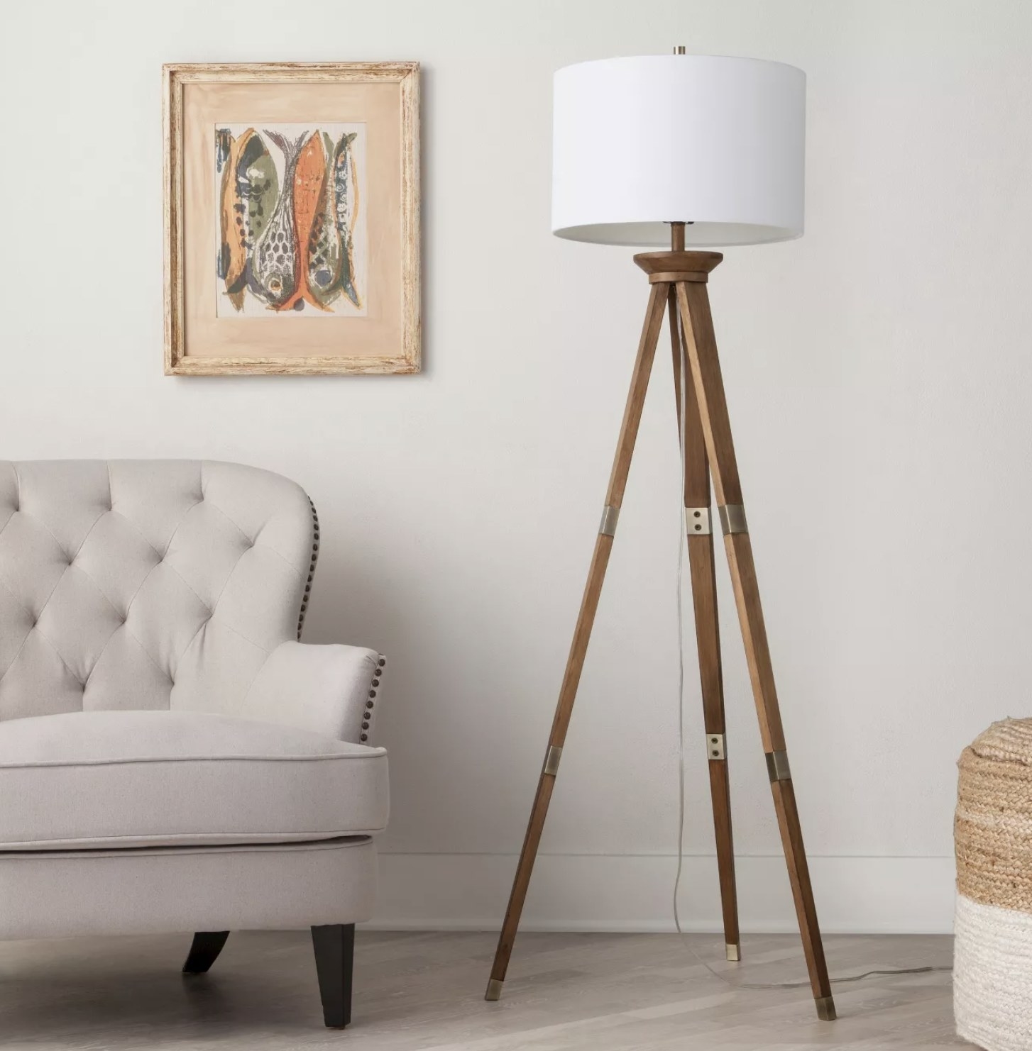 A wood tripod floor lamp in a living space with a white lamp shade