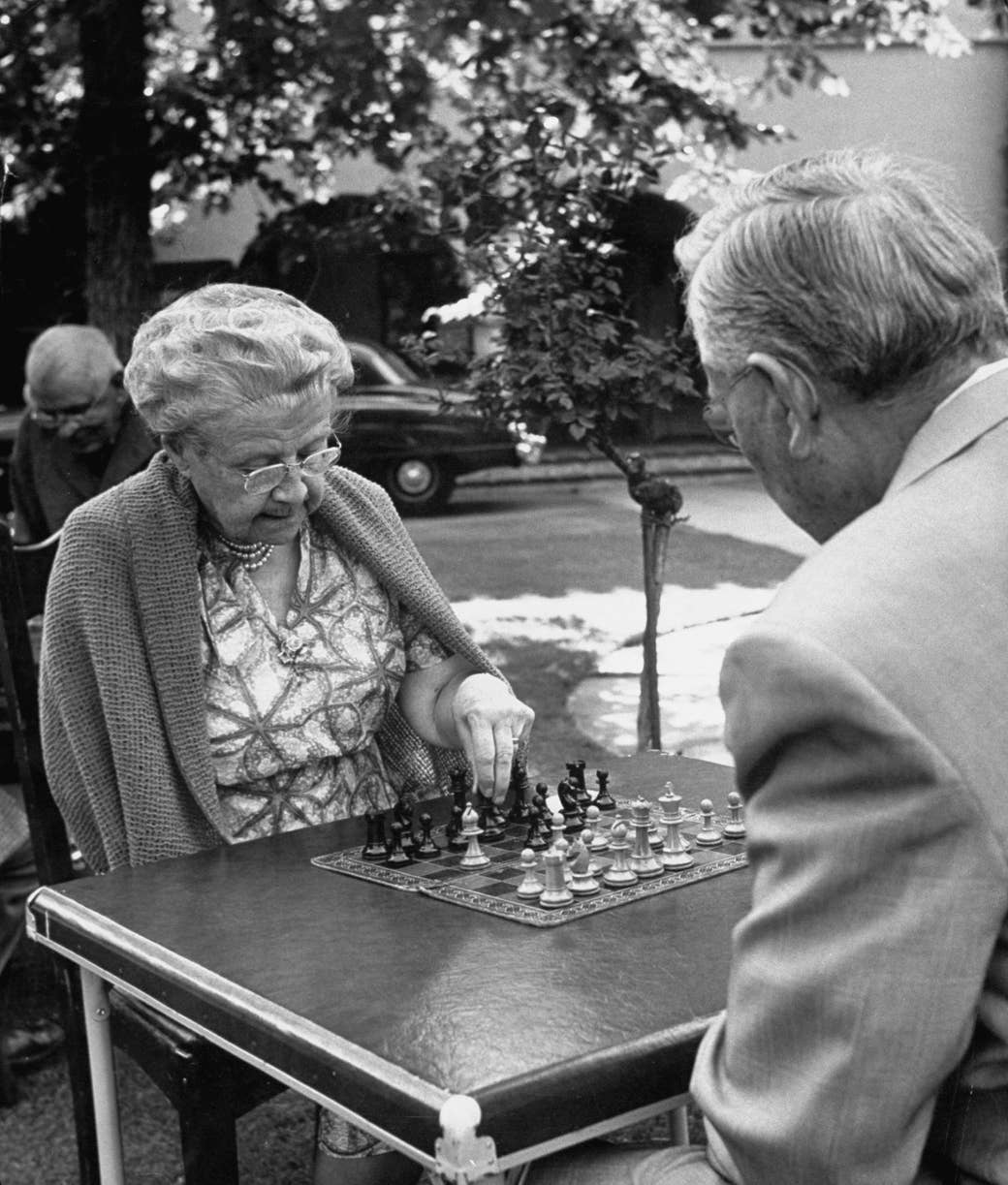 An older woman and an older man play chess outside on a sunny day