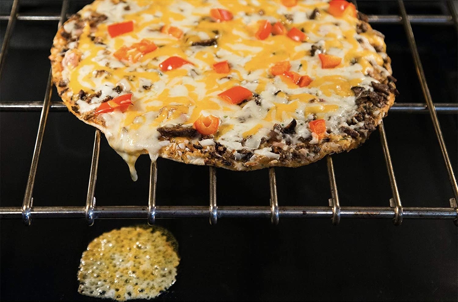 pizza in the oven with cheese dripped onto oven mat