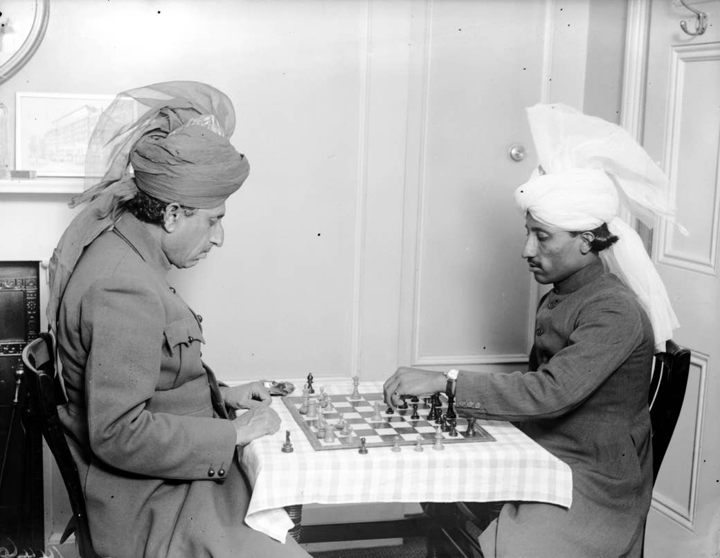 Two men in uniforms and turbans playing chess indoors