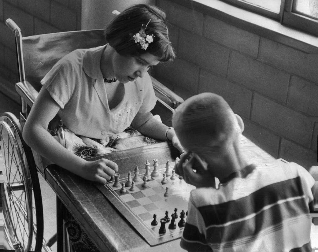 A girl in a wheelchair plays chess with a young boy