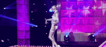 Drag queen Detox wearing a strappy white body harness and covered head to toe in silver body paint