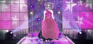 Drag queen Alaska dressed as a life size version of a doll she invented, wearing a pink dress and exaggerated makeup