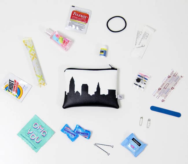 A small white faux leather pouch with a black skyline print surrounded by a mix of travel-sized toiletries and on-the-go essentials 