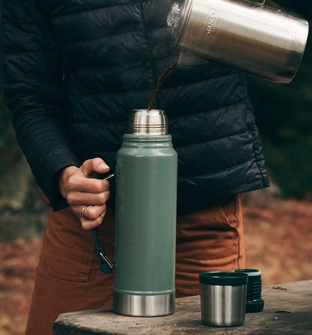A person pouring coffee from a kettle into a vacuum insulated thermos