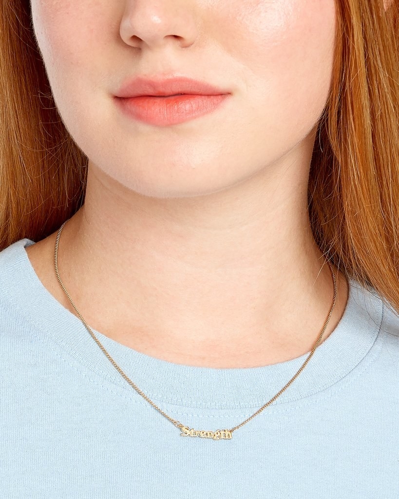 a model wearing the necklace that reads &quot;strength&quot; on a gold chain 