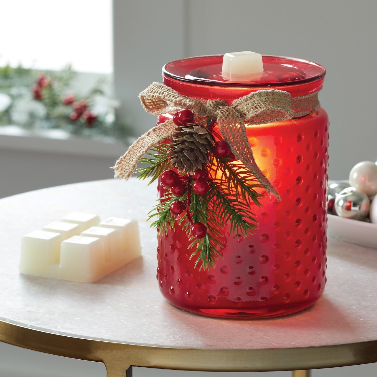 The red wax warmer decorated with a bow that has a small pinecone, red berries and pine needles