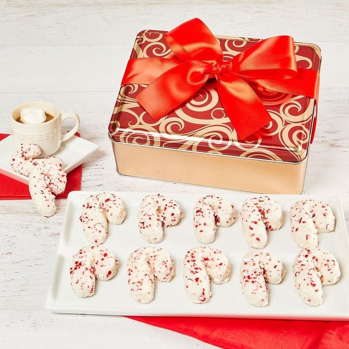 the candy cane cookies with white frosting and red peppermint flakes next to a gift box 