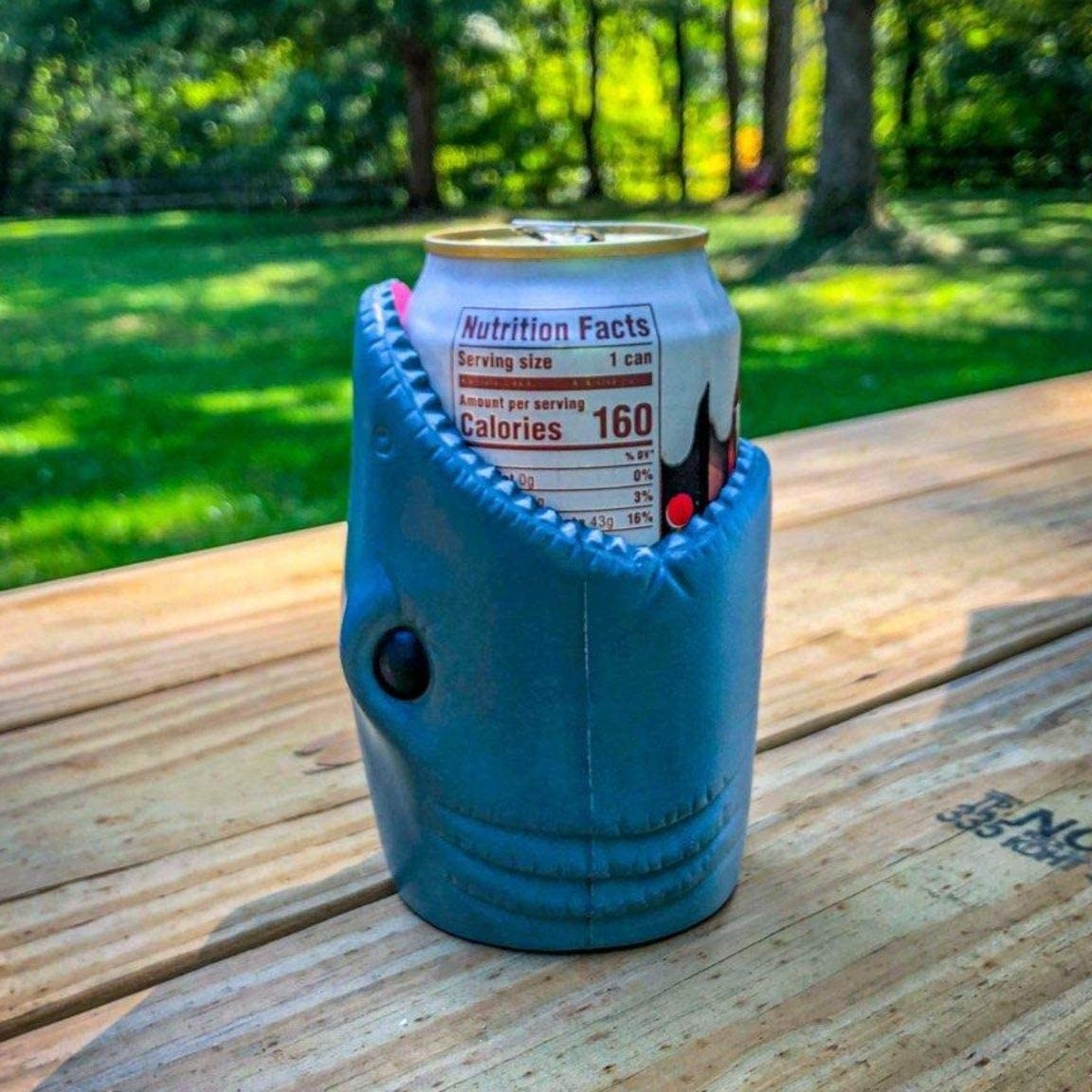 Shark mouth-shaped can holder with soda can inside of it on a picnic table