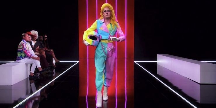 Drag queen Gigi Goode wearing a pastel pink, blue, and yellow motorcycle outfit with matching helmet
