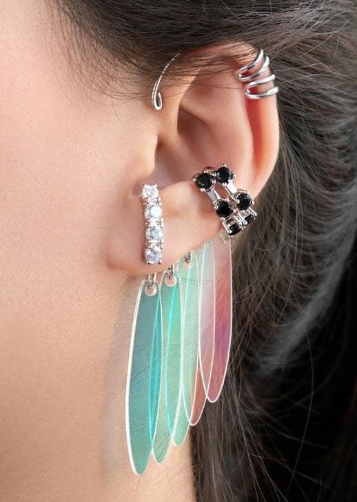 A set of three earring cuffs featuring jewels and colorful dangly parts designed like Harley Quinn&#x27;s earrings from Birds of Prey